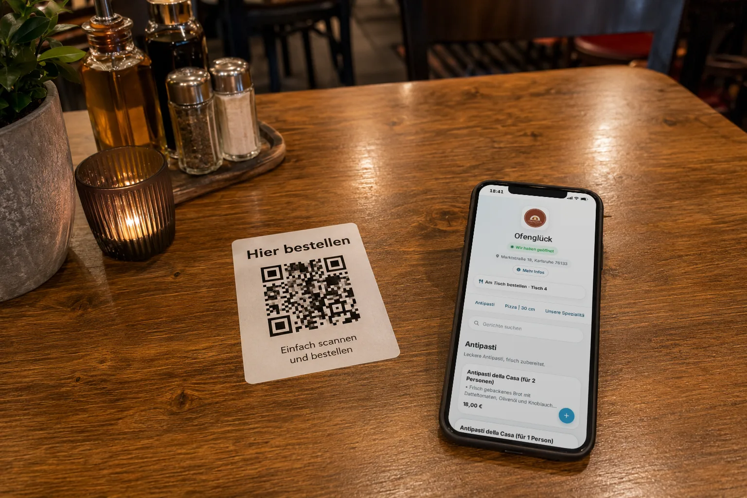 Restauranttisch mit QR-Code-Aufsteller „Hier bestellen" und Handy mit geöffneter Speisekarte