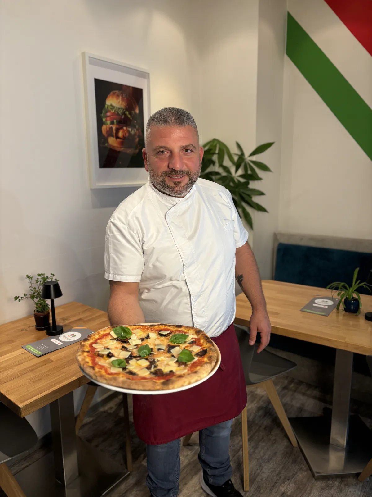 Enzo von Enzo’s Pizza mit einer Pizza in seinem Restaurant